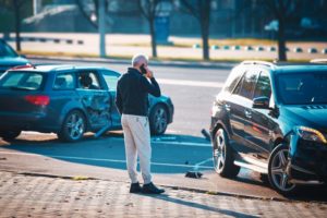 A man standing between two damaged vehicles while making a phone call
